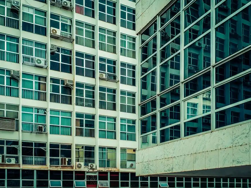 Converging urban buildings with reflective glass and numerous windows seen from below.